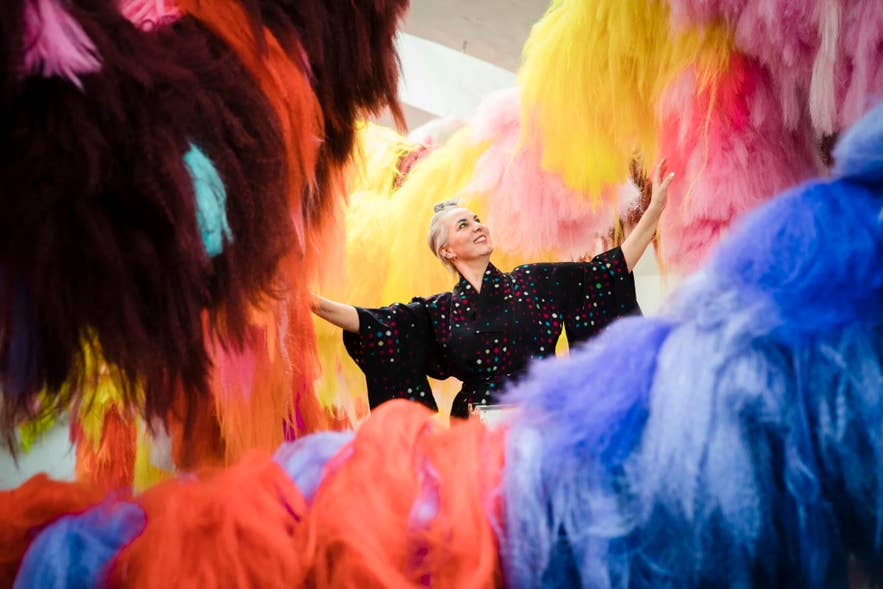 Icelandic artist Shoplifter standing among hanging colored synthetic hair pieces from her Chromo Sapiens installation.
