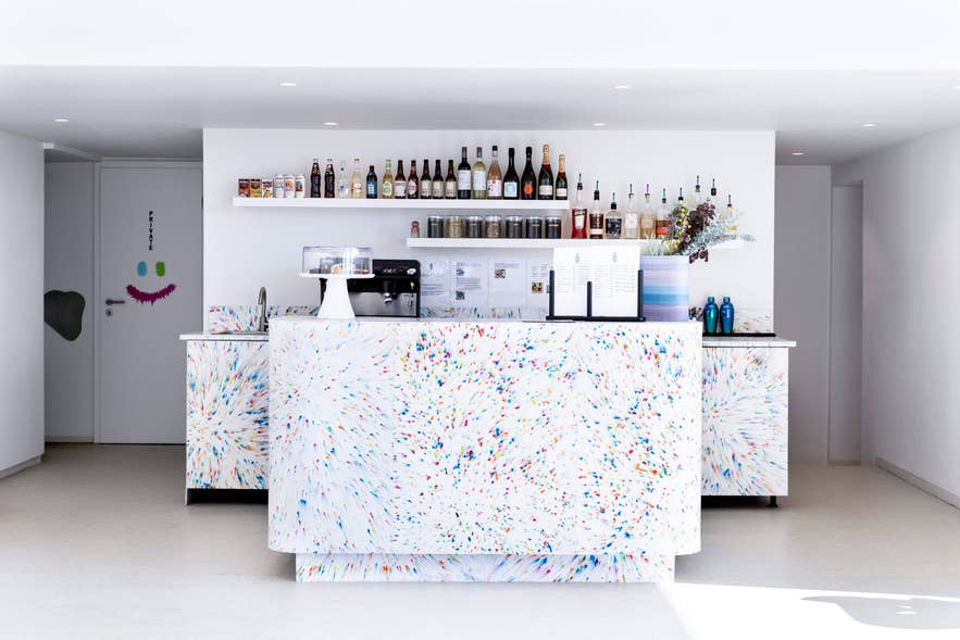 Bar counter at Hofudstodin's cafe, with a coffee machine and wine and spirit bottles on shelves above.