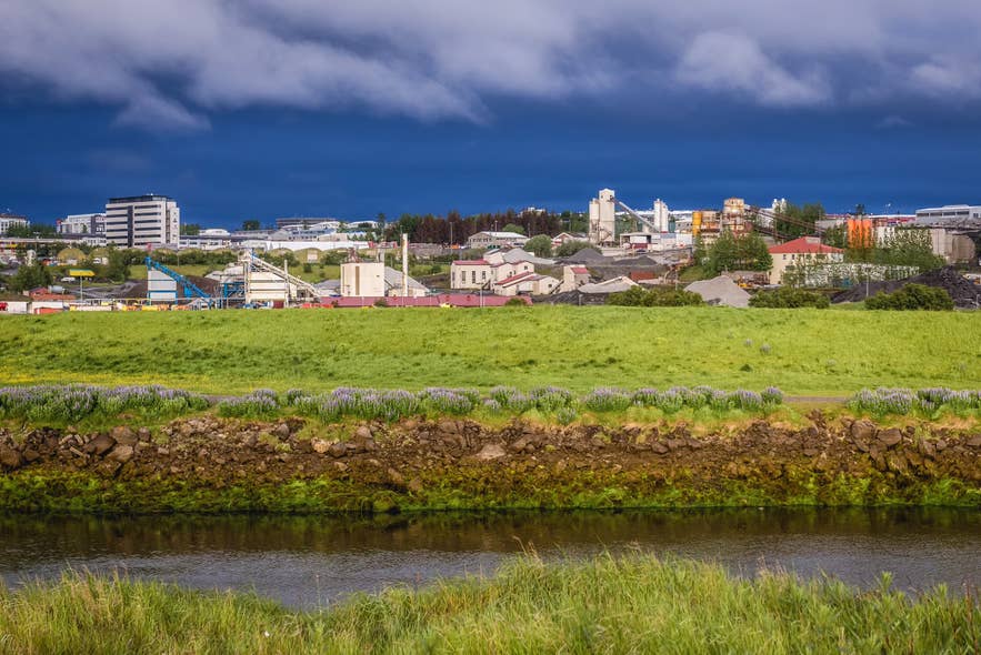 Industrial buildings and grassy riverbank in Reykjavik’s Ellidaardalur Valley.