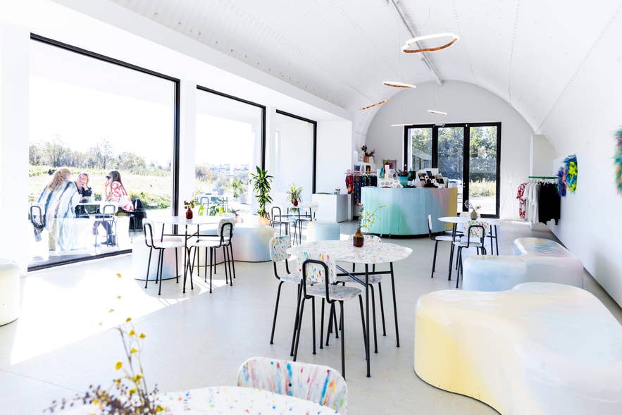 Hofudstodin's main interior with vaulted ceiling, terrazzo tables, and pastel furniture.