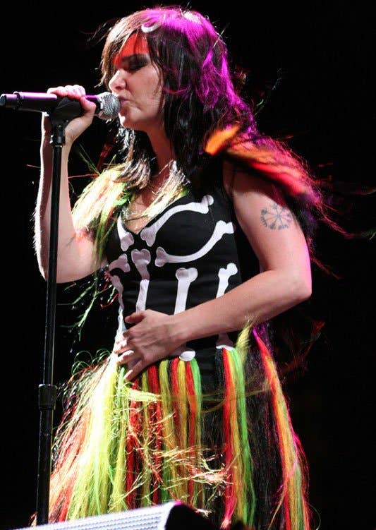 Icelandic artist Bjork singing on stage with colorful hair, showing a Vegvisir-style stave tattoo on her upper arm.