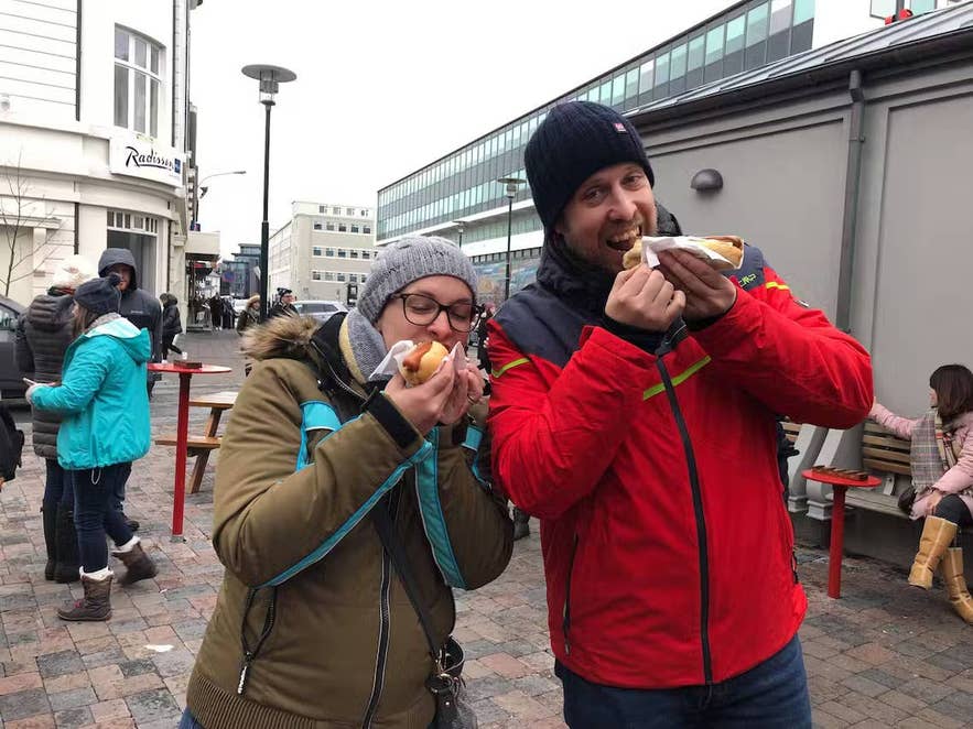 Travelers eating traditional Icelandic hot dogs on a Reykjavik street.