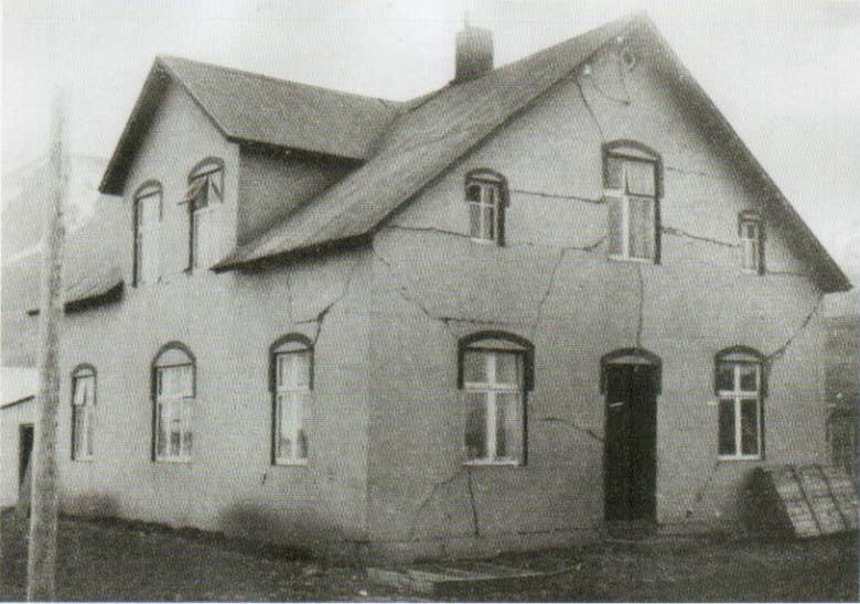 A black-and-white photo of a two-story house in Dalvik with large cracks across its facade from the 1934 earthquake.