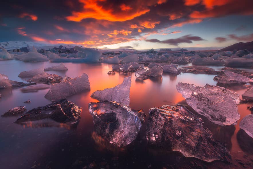 Icebergs floating on Jokulsarlon glacier lagoon beneath the burning red and orange sky of the midnight sun in South Iceland.
