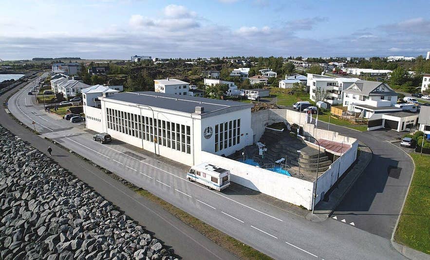 Aerial view of the Sundholl Hafnarfjardar swimming pool complex beside a coastal road