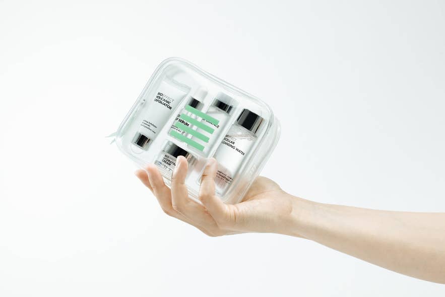 A hand holding a clear BIOEFFECT travel set with exfoliator, serum, cream, and cleansing water.