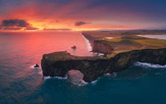 Sunset over the sea arch at Dyrholaey Cliffs on the South Coast of Iceland.