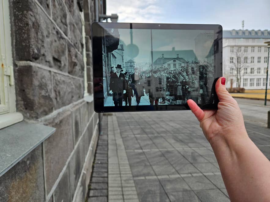 Hand holding a tablet overlaying a wartime photo onto a Reykjavik street on a World War II history tour.