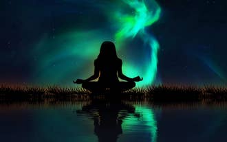 Northern lights glow above a meditating silhouette during an evening retreat session in South Iceland.
