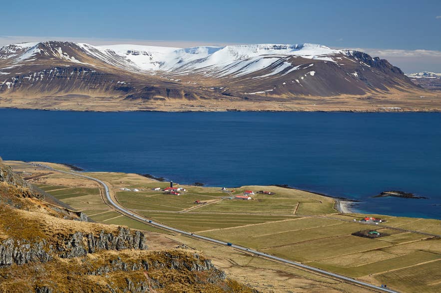 Snow-capped mountains across Hvalfjordur, with farmland and Route 47 in the foreground.