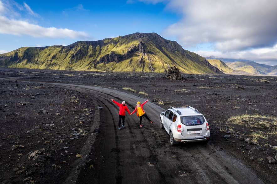 Travelers posing for the camera next to a 4x4 rental vehicle on an F-road in the Icelandic Highlands.