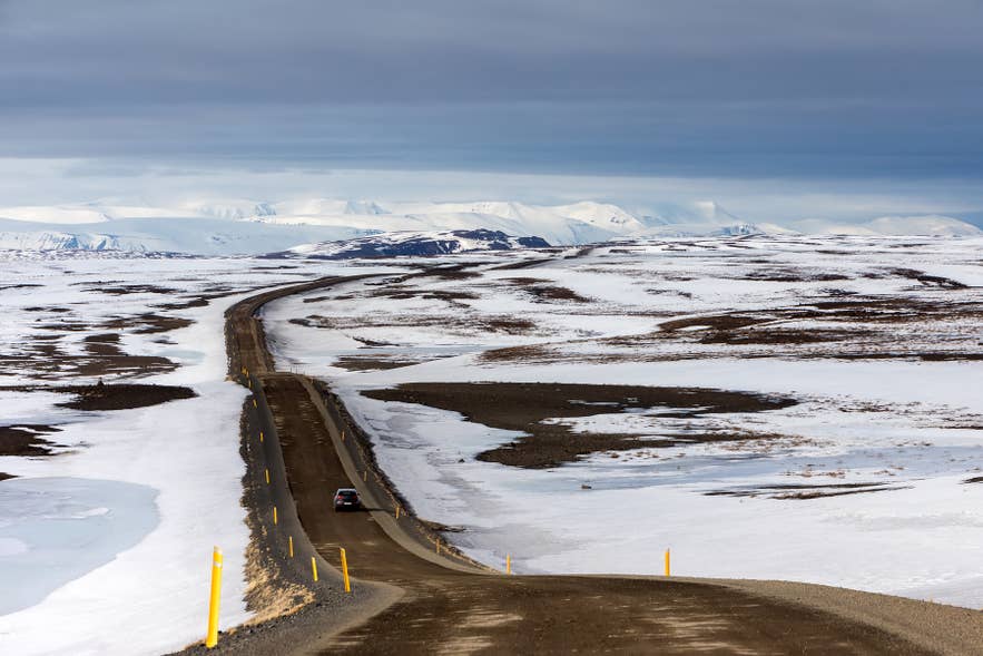 A car driving a long, snow-lined road in Iceland in winter, when wind closes roads most often from December to March. A car driving a long, snow-lined road in Iceland in winter, when wind closes roads most often from December to March.
