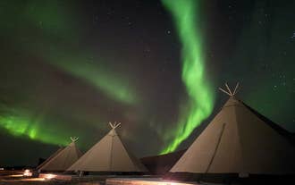 Northern lights glow green over a Nordic tipi at Sorla Camp glamping in South Iceland.