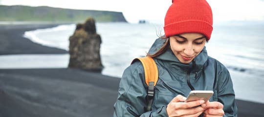 Woman traveler on Kirkjufjara Black Sand Beach using smartphone.jpg