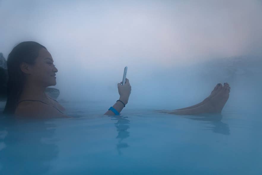 Woman using a smartphone in the steamy Blue Lagoon Geothermal Spa in Iceland Woman using a smartphone in the steamy Blue Lagoon Geothermal Spa in Iceland