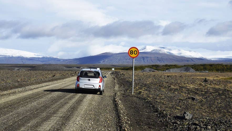 Small rental car on a gravel road in Iceland with a road sign and a glacier ahead