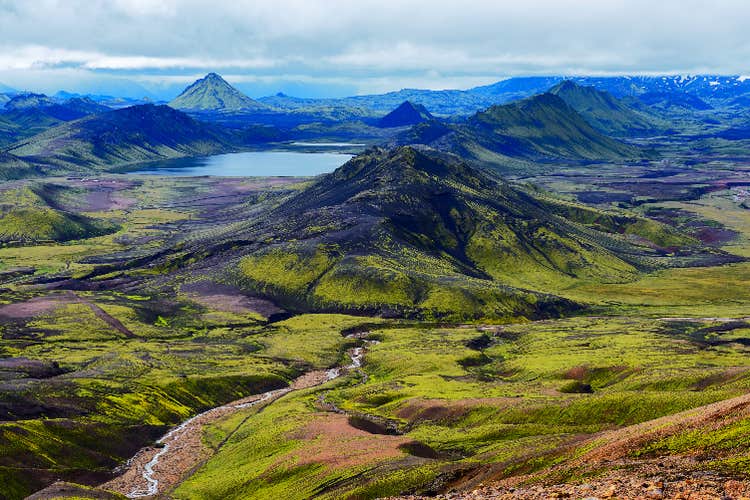 Mossy green mountain peaks with a lake in the distance.