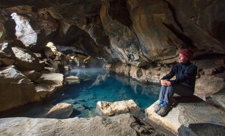 A woman sits beside the blue geothermal spring inside Grjotagja Cave near Lake Myvatn.