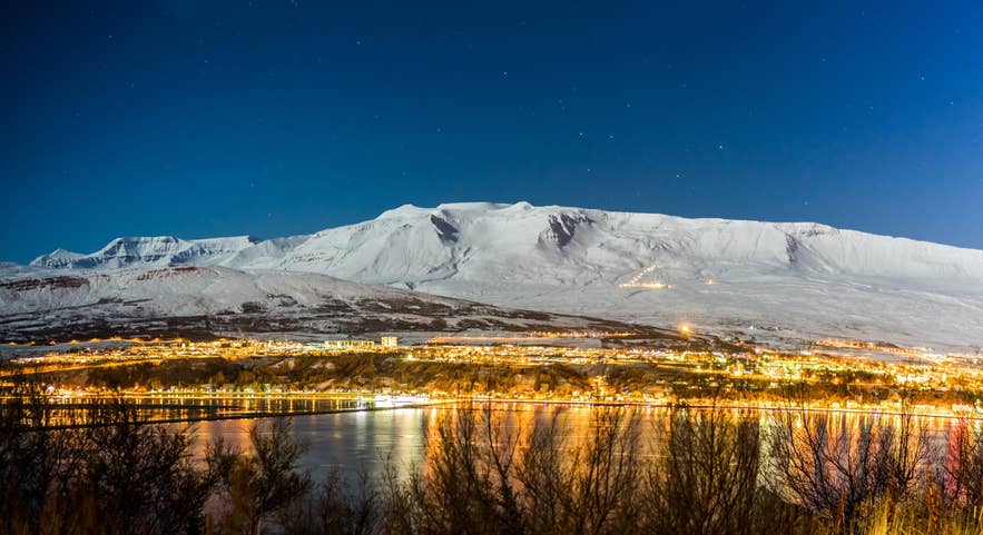 Town lights glow below a snow-capped mountain in Akureyri on a winter evening in North Iceland.
