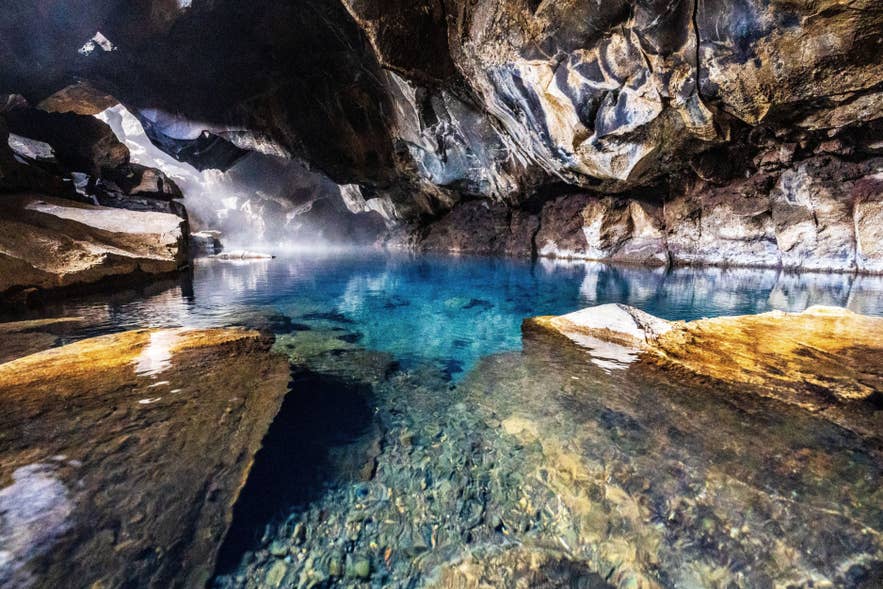 Steam rises over the clear turquoise geothermal pool inside Grjotagja Cave in North Iceland.