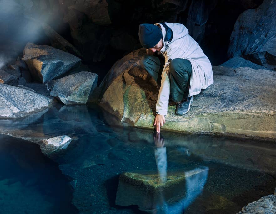 A visitor tests the warm water of the geothermal spring inside Grjotagja Cave in North Iceland.