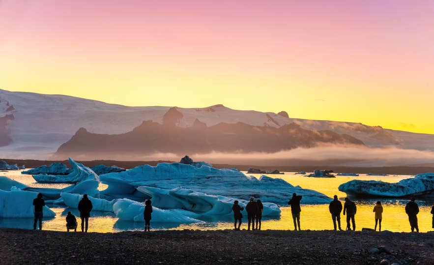 Travelers watching icebergs at Jokulsarlon Glacier Lagoon under a golden sunset sky.