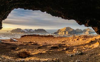 A rock arch on Heimaey Island frames a view of distant mountains in Vestmannaeyjar.