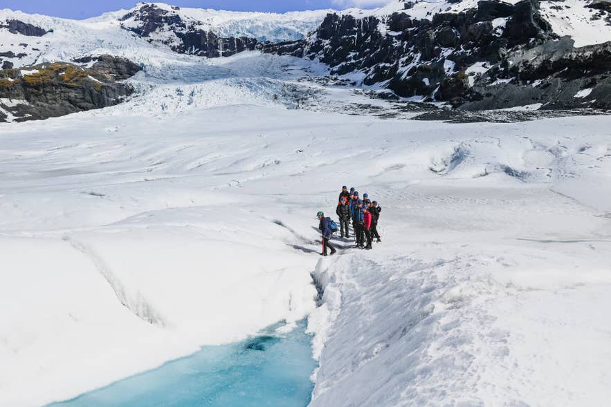 Guided tour group beside a turquoise meltwater channel on Falljokull Glacier below its icefall.