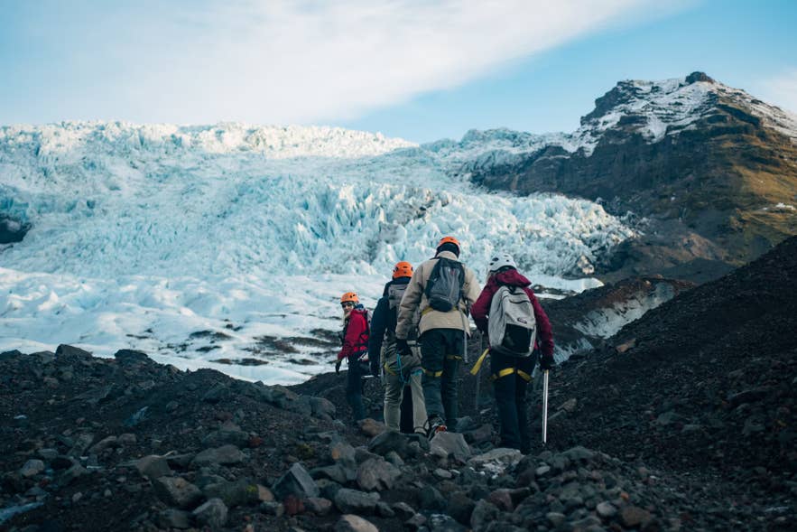 Hikers crossing the rocky moraine toward Falljokull Glacier below its dark flanking ridge.