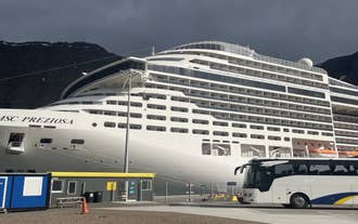 A shuttle bus and a cruise ship docked at Isafjordur Historic Harbour beneath the Westfjords mountains.
