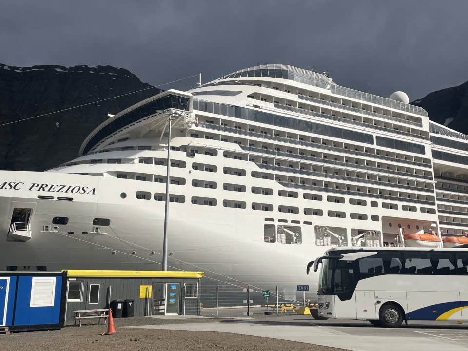 A shuttle bus and a cruise ship docked at Isafjordur Historic Harbour beneath the Westfjords mountains.