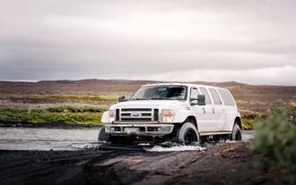 A white super jeep fords a shallow river on a 4x4 shore excursion through North Iceland near Akureyri.