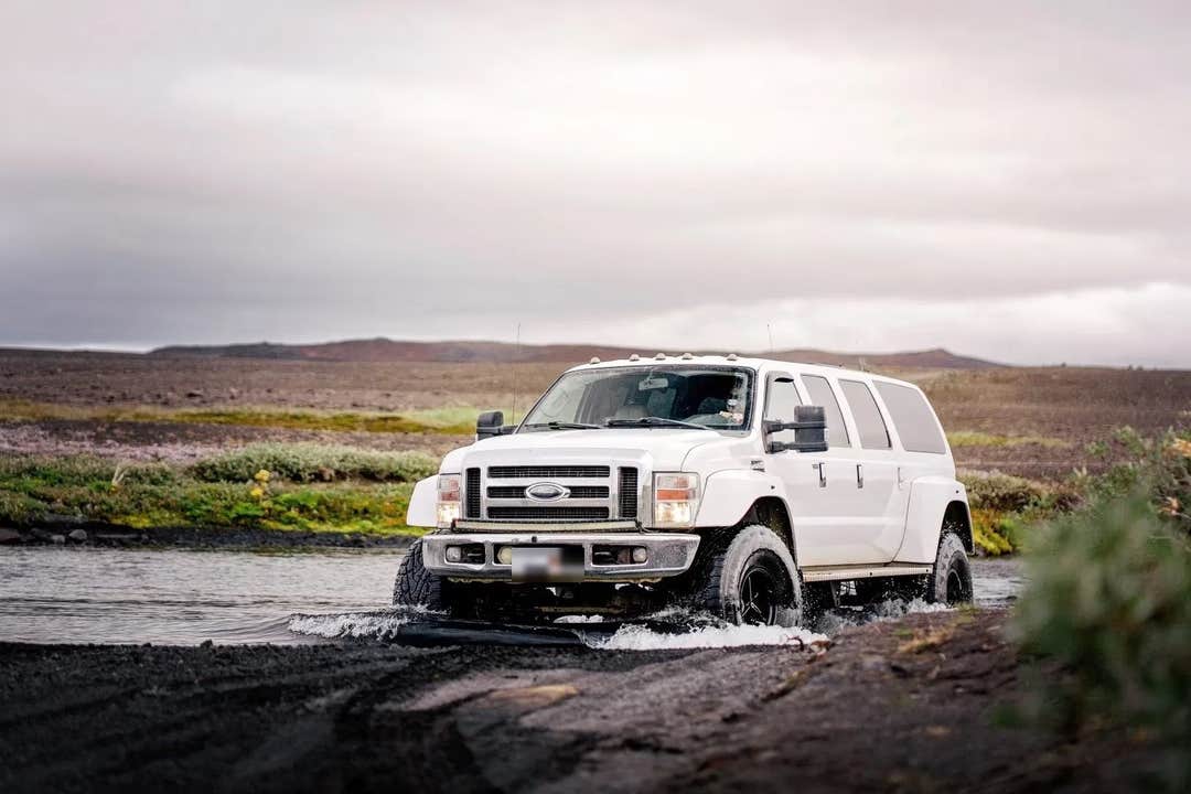 A white super jeep fords a shallow river on a 4x4 shore excursion through North Iceland near Akureyri.