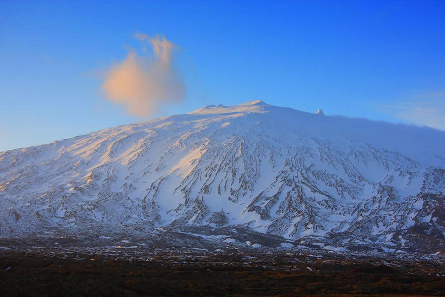 Snow-covered Snaefellsjokull Volcano glowing at sunset beneath a plume of cloud. Snow-covered Snaefellsjokull Volcano glowing at sunset beneath a plume of cloud.