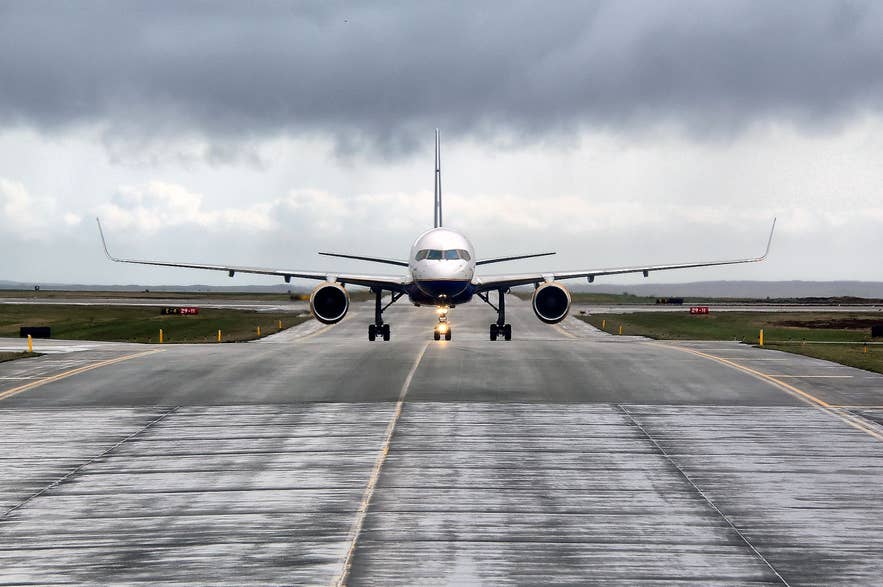 Passenger plane taxiing on a wet runway at Keflavik International Airport under dark clouds.