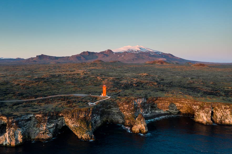 Orange Svortuloft Lighthouse on sea cliffs at the tip of Snaefellsnes, with Snaefellsjokull behind.
