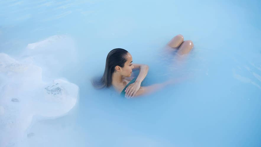 Two women enjoying face masks at the Blue Lagoon in Iceland with moss in the background.