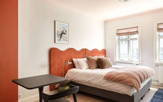 Bedroom with a curved terracotta headboard and white linens in the Collector´s House by Muse