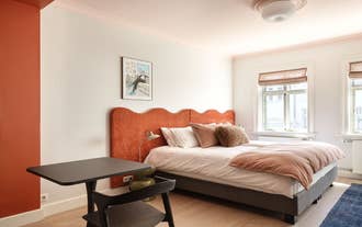 Bedroom with a curved terracotta headboard and white linens in the Collector´s House by Muse