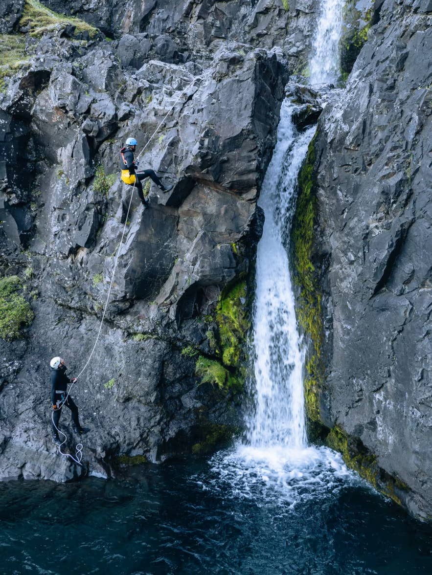 Canyoneers abseil down basalt cliffs beside a waterfall on a canyoning tour in Vatnajokull National Park.