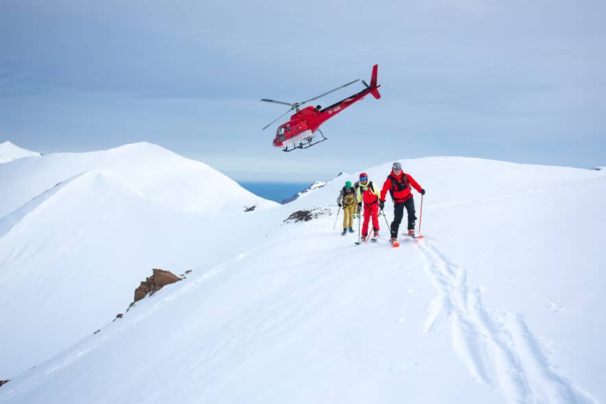 A helicopter hovers above skiers on a snowy Troll Peninsula ridge during a heli-skiing tour in North Iceland.