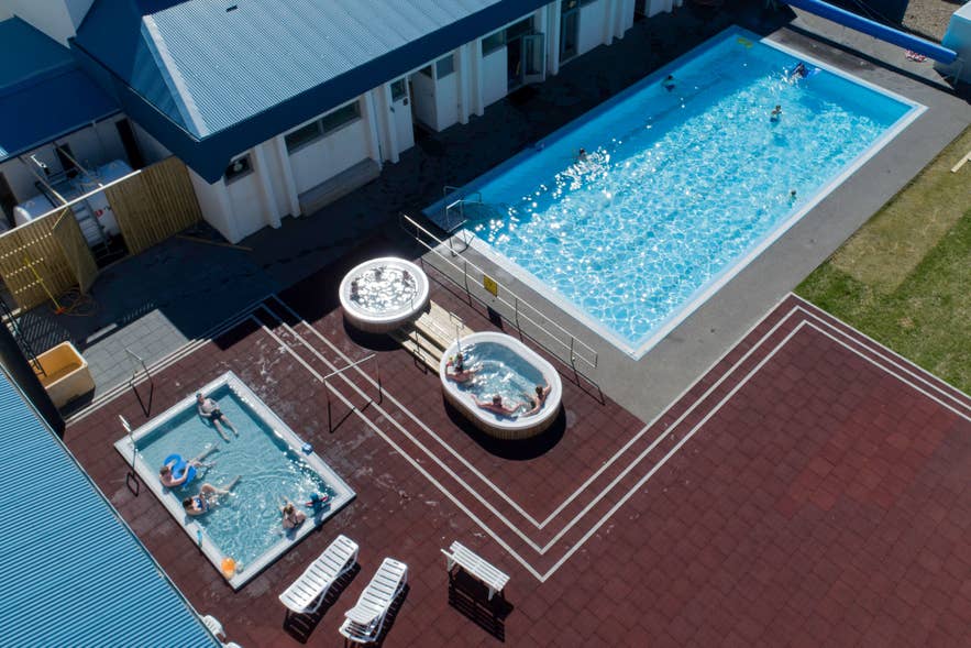 Aerial view of the Grundarfjordur swimming pool, with bathers in its hot tubs and a children's pool on a sunny day.