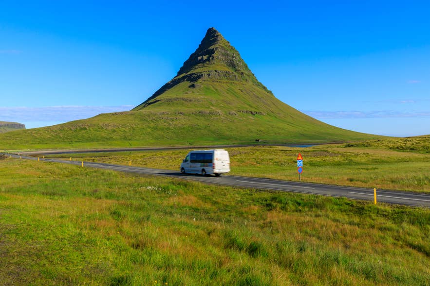 A minibus drives past the green slopes of Kirkjufell on a summer day tour of Snaefellsnes.