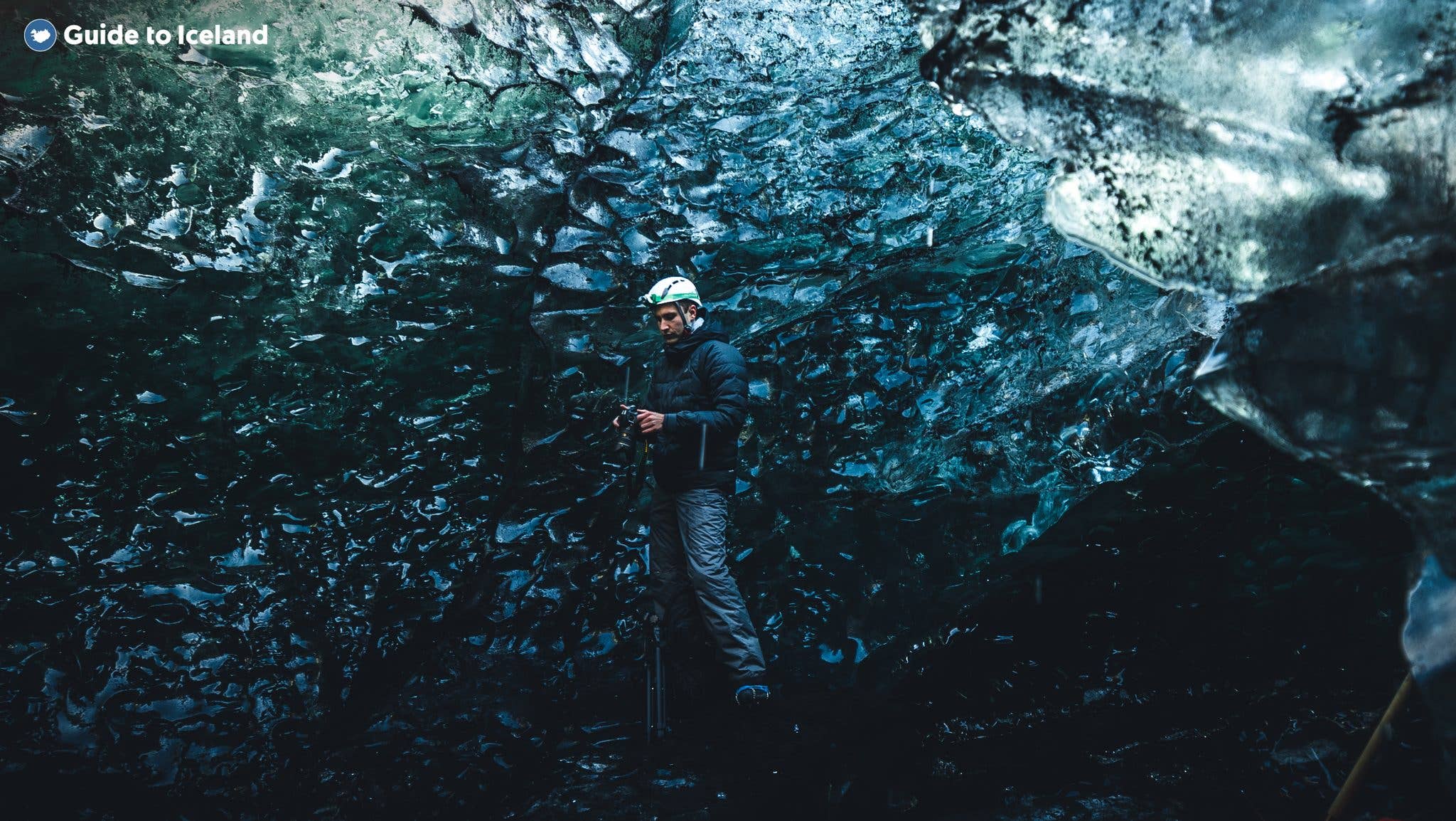 A visitor pauses with an ice axe inside a rugged, dark-blue ice cave beneath Vatnajökull glacier in southeast Iceland.