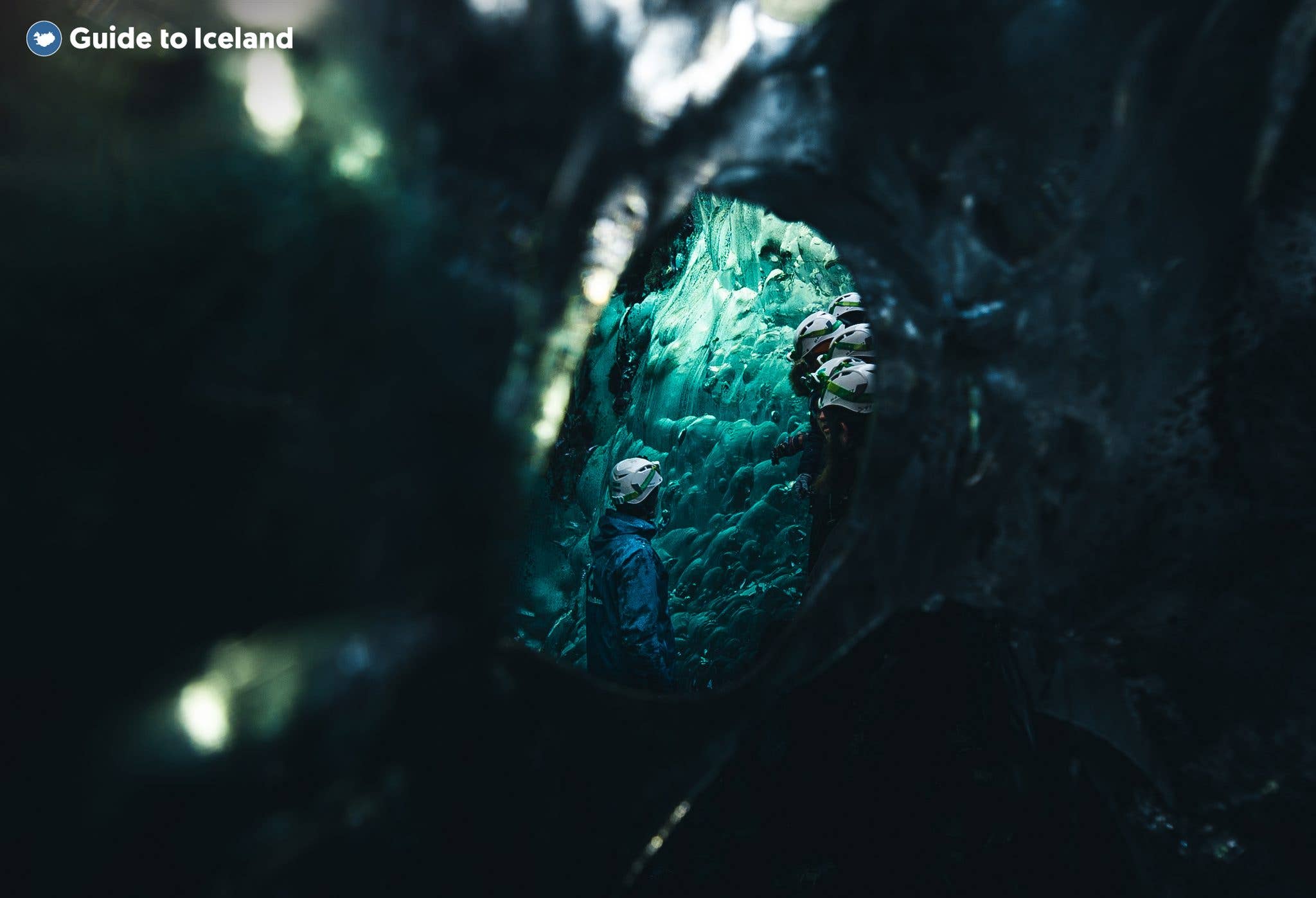Daylight glows through a round opening in a green-and-blue ice cave under Vatnajökull glacier, Iceland.