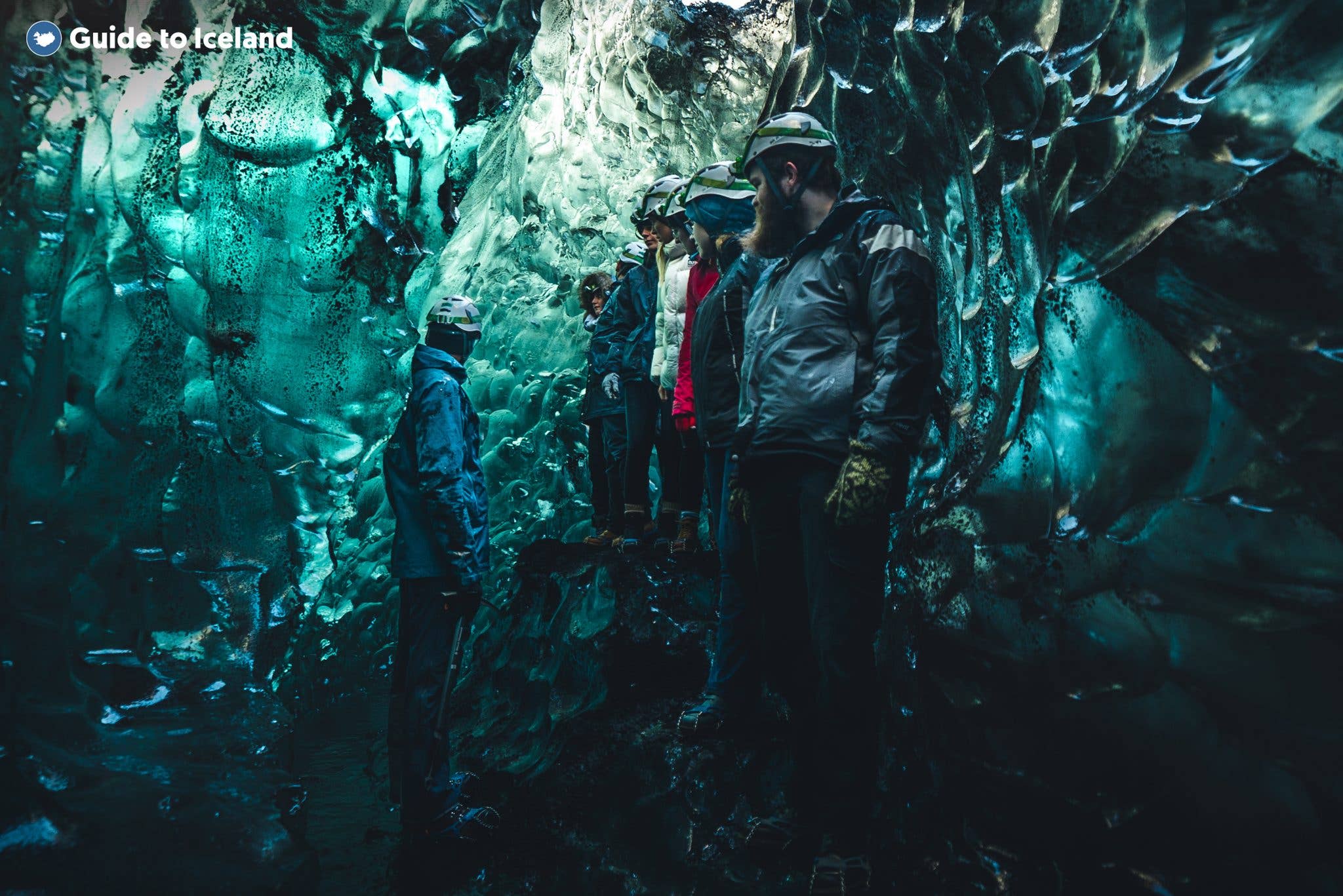 A guided group in helmets explores a spacious turquoise ice cave in Vatnajökull glacier, southeast Iceland.