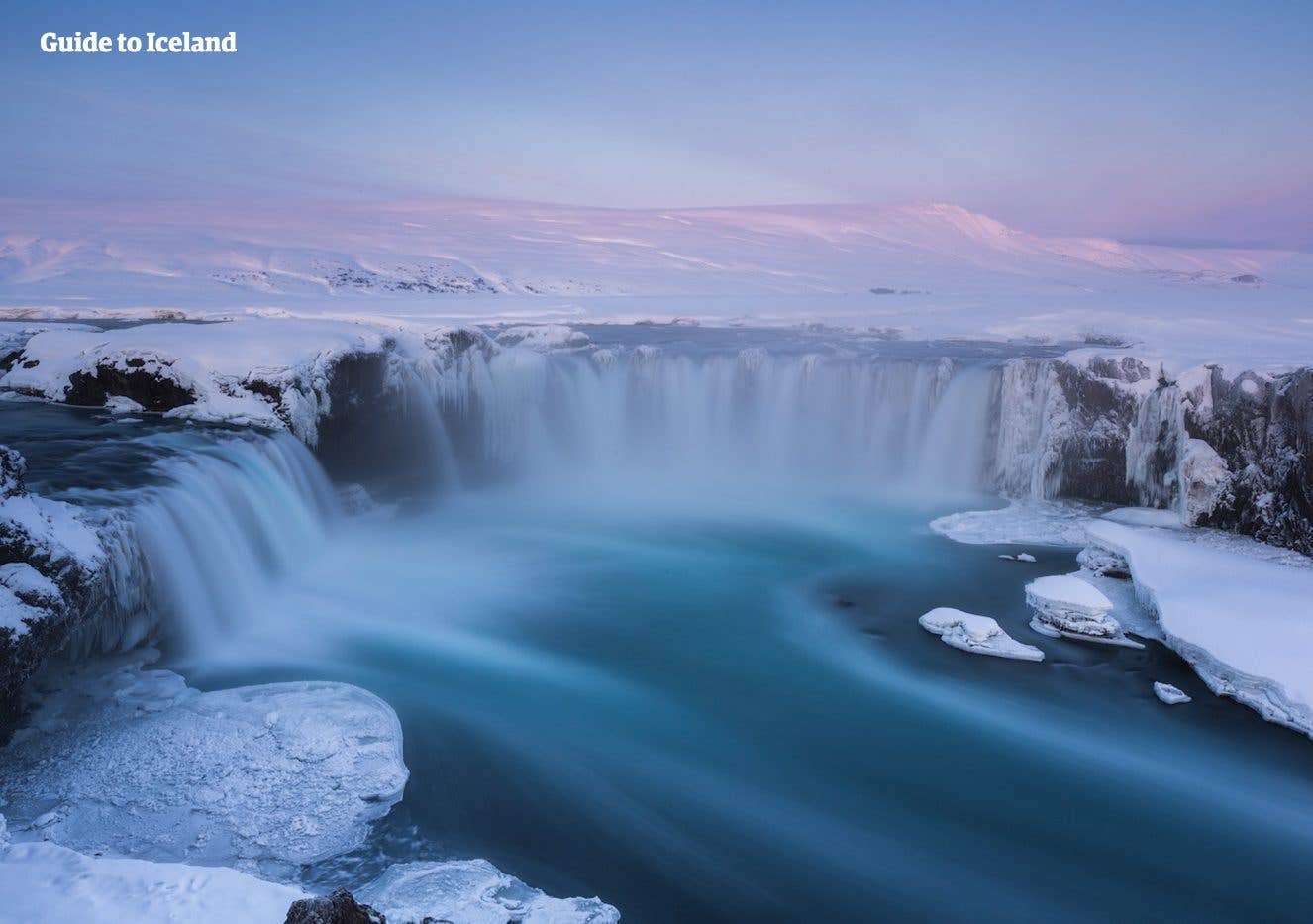 Goðafoss, the "waterfall of the gods", flows between snow-covered banks under a soft winter sky in North Iceland.