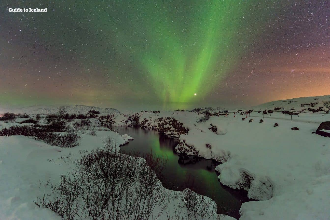 Green and purple aurora reflect in a partly frozen river at Þingvellir National Park in southwest Iceland.