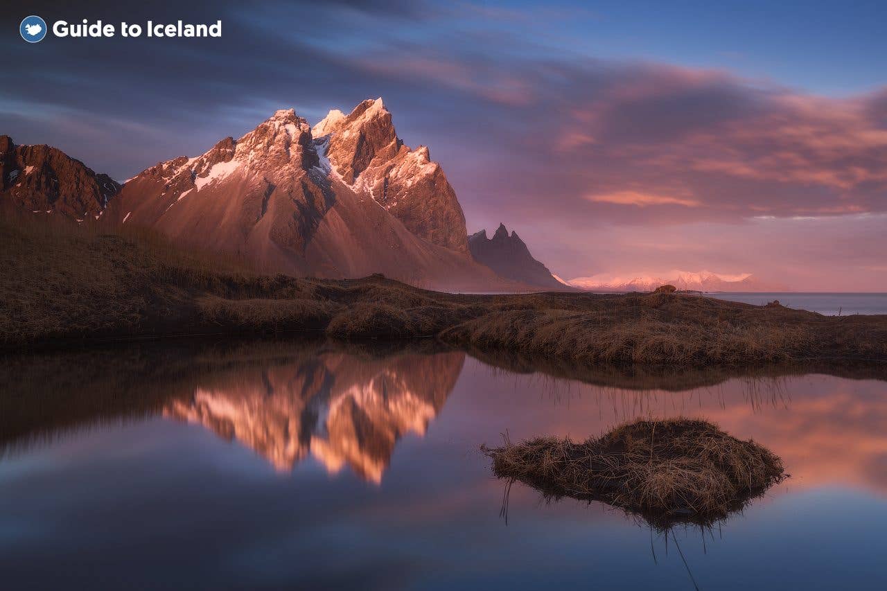 The jagged peaks of Vestrahorn glow pink at sunset, mirrored in a still lagoon on the Stokksnes headland in southeast Iceland.