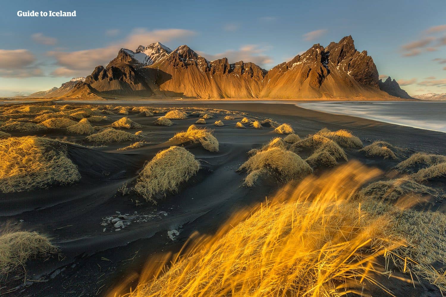 Golden grass and black-sand dunes stretch beneath the sharp ridges of Vestrahorn mountain at Stokksnes, southeast Iceland.